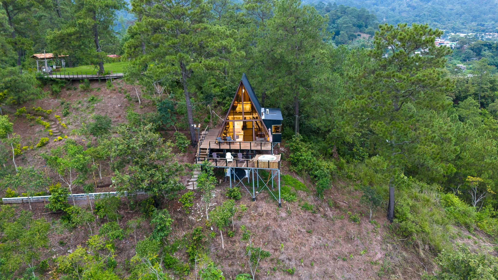Vista aérea de la cabaña en lo alto de la ladera, rodeada de bosque de pinos