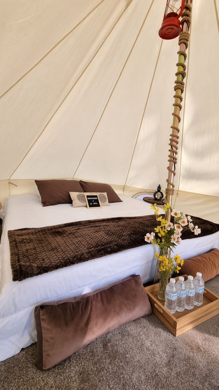 Interior de una tienda de glamping con cama y cojines