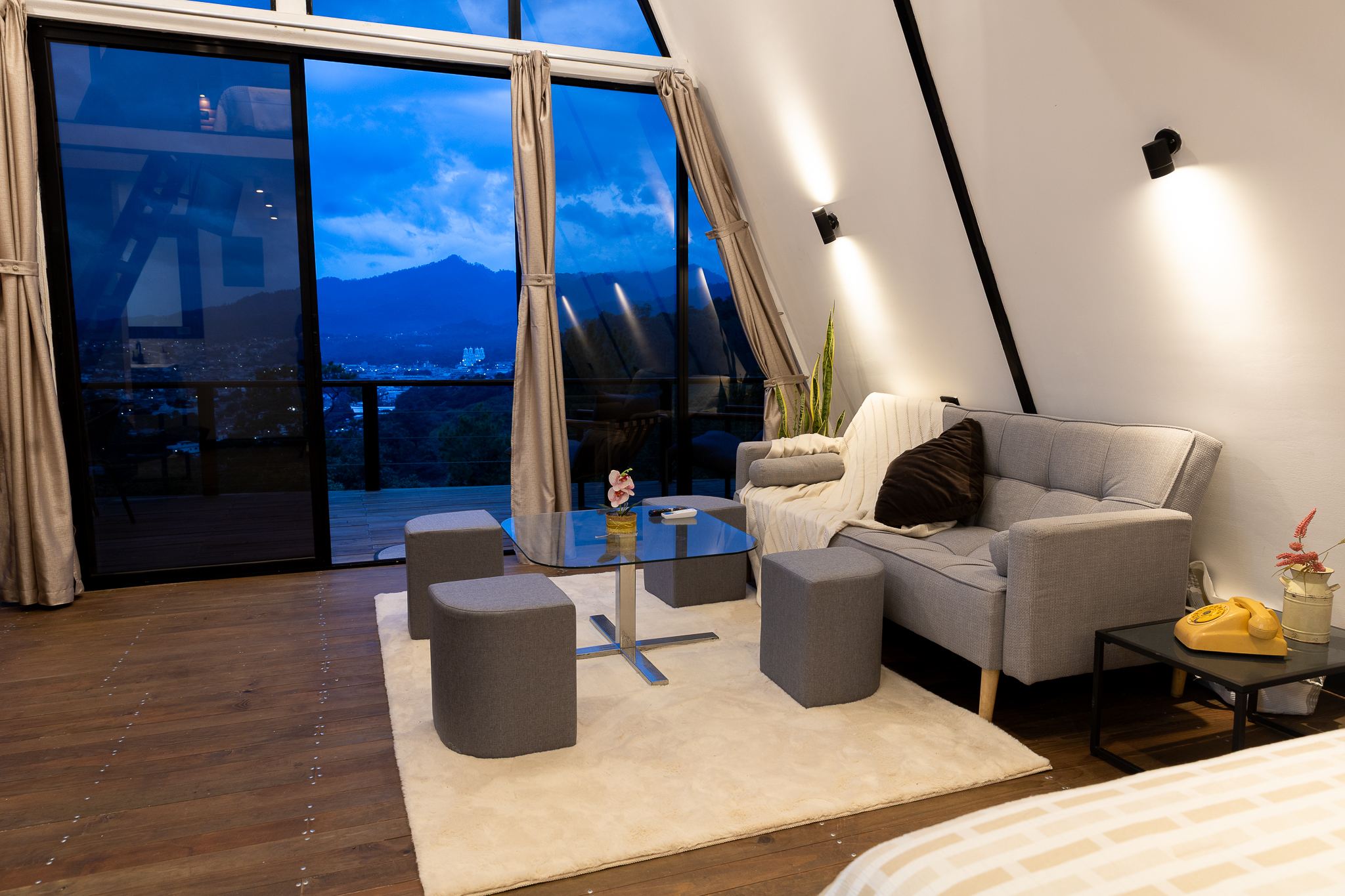 Sala de la cabaña con ventanales de piso a techo y vista a las montañas al atardecer